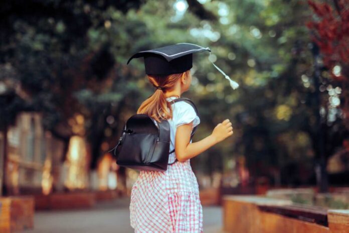 Little,Girl,Wearing,A,School,Bag,And,A,Mortarboard.,Happy