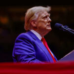 NATO Allies Split: Reject Trump’s Peace Plan A man in a blue suit and red tie speaking into a microphone on stage