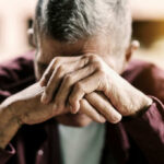 Elderly man with hands covering his face, expressing emotional distress