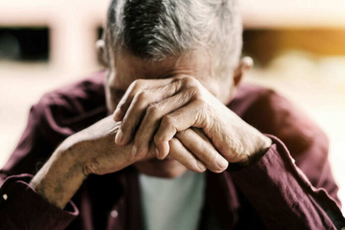 Elderly man with hands covering his face, expressing emotional distress