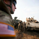 Iranian Drone Strike Shakes US Military Soldiers in military gear coordinating near armored vehicles during training