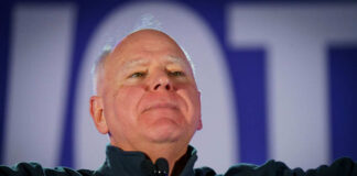 Man in a dark jacket speaking passionately at a podium with a microphone
