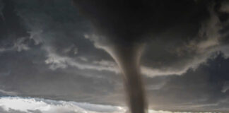 A tornado forming under dark storm clouds in a rural landscape