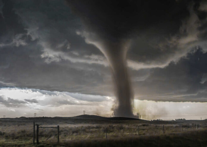 A tornado forming under dark storm clouds in a rural landscape
