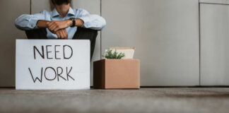 Person sitting on the ground holding a sign that says 'NEED WORK'