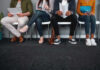 A diverse group of people sitting in a waiting area, each engaged with their devices or documents