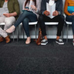 A diverse group of people sitting in a waiting area, each engaged with their devices or documents
