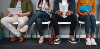 A diverse group of people sitting in a waiting area, each engaged with their devices or documents