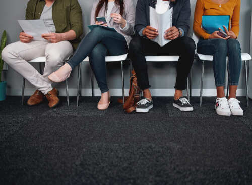A diverse group of people sitting in a waiting area, each engaged with their devices or documents
