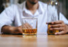 A man holding a whiskey glass and a bottle in a bar setting