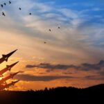 Massive Military Moves – Iran Hits Kurdish Bases Silhouette of missiles against a colorful sunset with birds flying