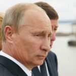 Putin’s Gas Threat: EU Faces Energy Chaos Close-up of a serious-looking man in a suit at an outdoor event near water