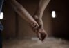 Two hands holding each other in a dimly lit room