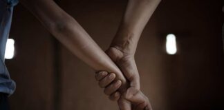Two hands holding each other in a dimly lit room