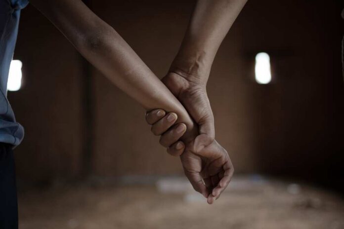 Two hands holding each other in a dimly lit room