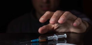 A hand reaching for a syringe next to a pile of white powder