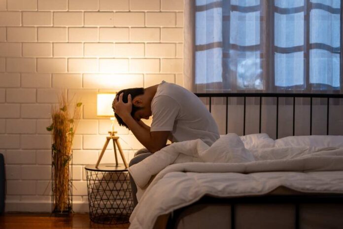shutterstock_2436660863.jpg A person sitting on a bed with their head in their hands, expressing distress