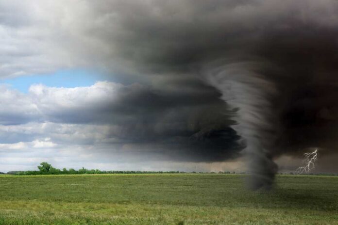 A tornado forming under dark storm clouds in an open field