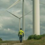 A worker in a yellow jacket walking among wind turbines