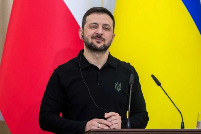 A political leader speaking at a press conference with flags in the background
