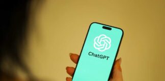 A person holding a smartphone displaying the ChatGPT logo on a teal background