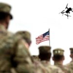 Military personnel standing in formation with a drone flying overhead and an American flag in the background