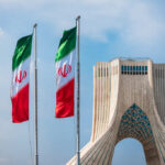 Iran Boasts: Enough Uranium for 11 Nukes? Three Iranian flags in front of the Azadi Tower against a blue sky