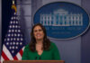 A woman in a green dress smiling at a podium in front of the White House seal