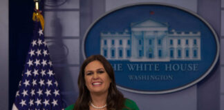 A woman in a green dress smiling at a podium in front of the White House seal