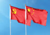 Two flags, one with the Communist Party symbol and the other with the Chinese national emblem, waving against a blue sky