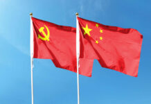 Two flags, one with the Communist Party symbol and the other with the Chinese national emblem, waving against a blue sky