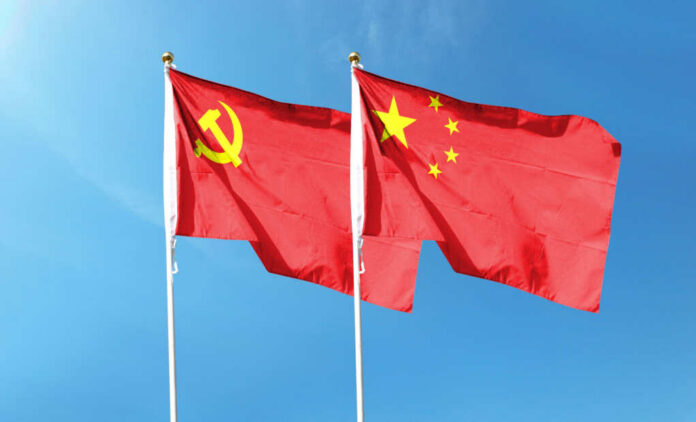 Two flags, one with the Communist Party symbol and the other with the Chinese national emblem, waving against a blue sky