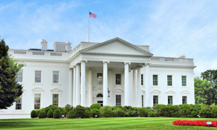 The White House with an American flag flying above, surrounded by greenery