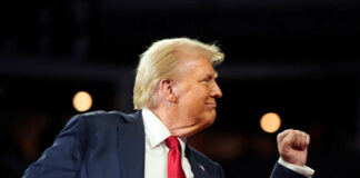 A man in a suit making a celebratory gesture during a speech