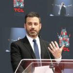 A man in a suit speaking at a podium during an event at TCL Chinese Theatre