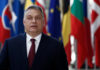 Election Turmoil: Orbán’s Rule on the Brink A political leader standing in front of various national flags