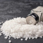 A glass salt shaker tipped over with salt spilling out