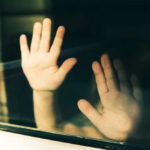 Child's hands pressed against a window, creating a reflective image