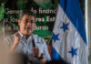 A speaker passionately addressing an audience with the Honduran flag in the background