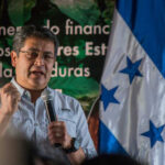 A speaker passionately addressing an audience with the Honduran flag in the background