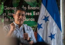 A speaker passionately addressing an audience with the Honduran flag in the background