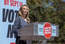 Trump Cabinet Firings: California’s First Partner Slams Back Speaker at a podium addressing a crowd at a political rally
