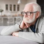 Elderly man with glasses resting his chin on his hand, looking thoughtfully