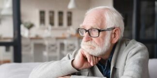 Elderly man with glasses resting his chin on his hand, looking thoughtfully