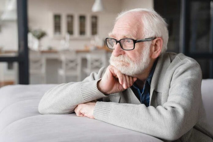 Elderly man with glasses resting his chin on his hand, looking thoughtfully