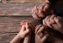 25,000 Christians FACE Harsh Eviction – No Plan! Multiple hands clasped together on a wooden surface