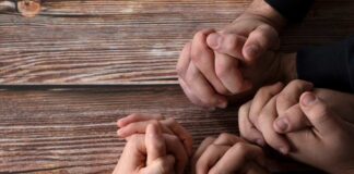 Multiple hands clasped together on a wooden surface
