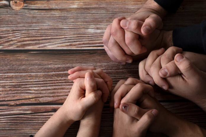 Multiple hands clasped together on a wooden surface