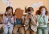 Four children sitting together, each engaged with their electronic devices