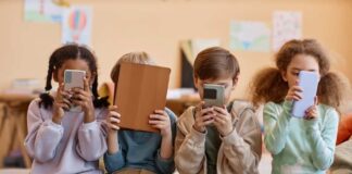 Four children sitting together, each engaged with their electronic devices